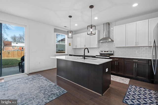 kitchen with wall chimney exhaust hood, sink, stainless steel range with electric cooktop, pendant lighting, and a kitchen island with sink