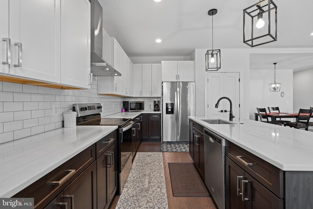 kitchen featuring pendant lighting, sink, wall chimney range hood, stainless steel appliances, and white cabinets