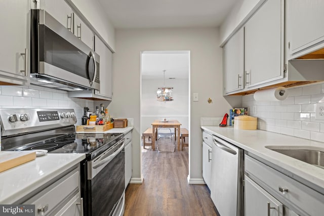 kitchen featuring tasteful backsplash, dark wood-type flooring, a chandelier, and appliances with stainless steel finishes