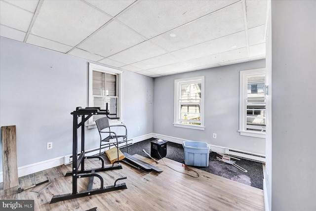 exercise room featuring wood-type flooring, a drop ceiling, and baseboard heating