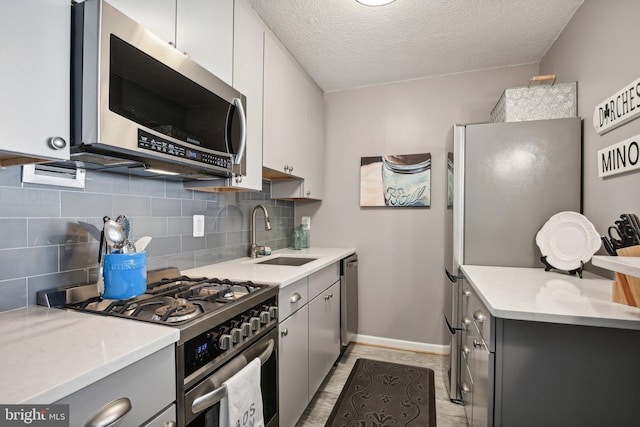 kitchen with appliances with stainless steel finishes, tasteful backsplash, white cabinetry, sink, and a textured ceiling