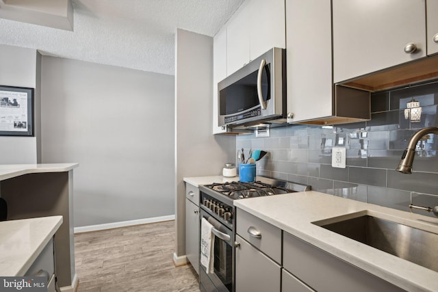 kitchen with sink, appliances with stainless steel finishes, white cabinetry, a textured ceiling, and decorative backsplash