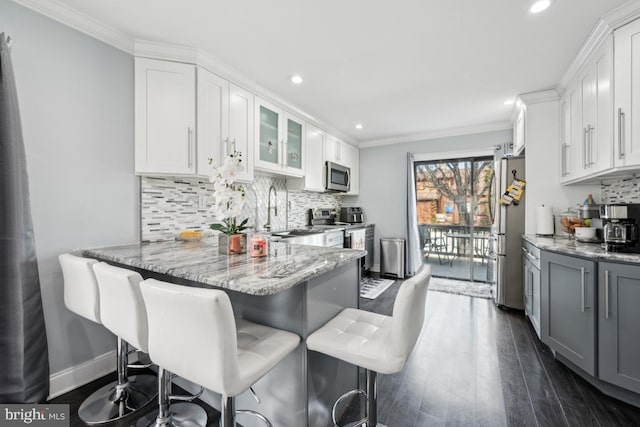 kitchen featuring appliances with stainless steel finishes, sink, a breakfast bar area, white cabinets, and light stone counters