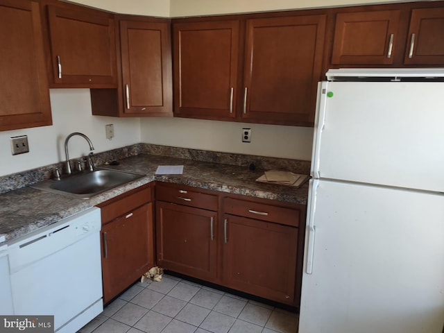 kitchen with sink, light tile patterned floors, white appliances, and dark stone counters