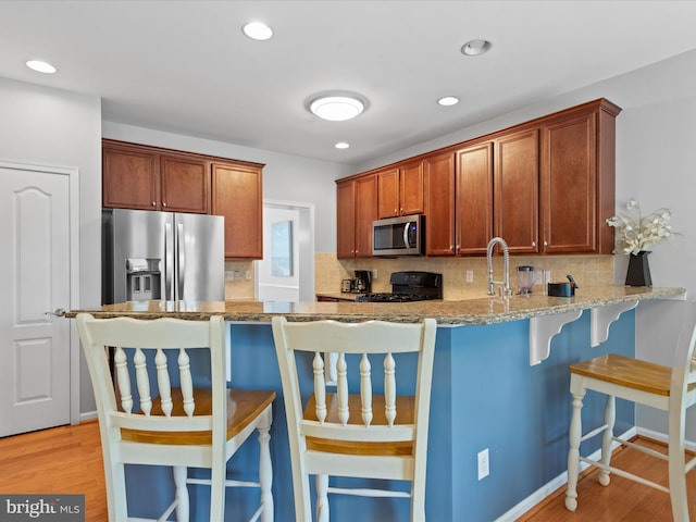 kitchen with a kitchen breakfast bar, kitchen peninsula, stainless steel appliances, light stone countertops, and light wood-type flooring