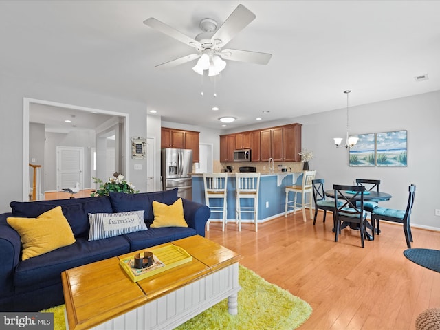 living room featuring ceiling fan with notable chandelier and light wood-type flooring