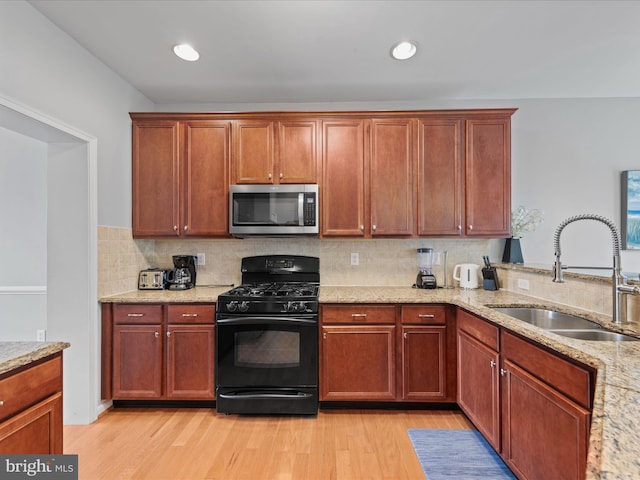 kitchen with sink, decorative backsplash, black gas stove, light stone countertops, and light wood-type flooring