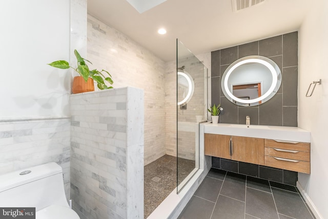 bathroom featuring a tile shower, tile walls, vanity, toilet, and tile patterned floors