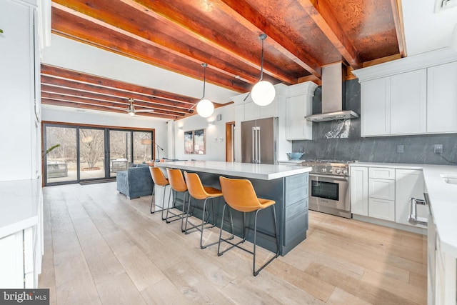 kitchen featuring a kitchen island, high quality appliances, white cabinets, hanging light fixtures, and wall chimney exhaust hood