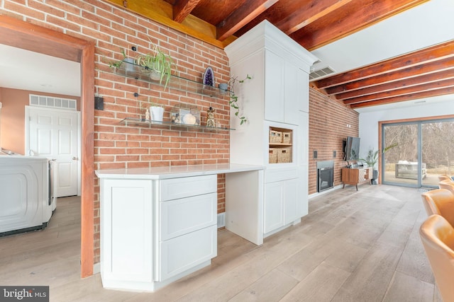 kitchen with beam ceiling, washer / dryer, light wood-type flooring, and white cabinets