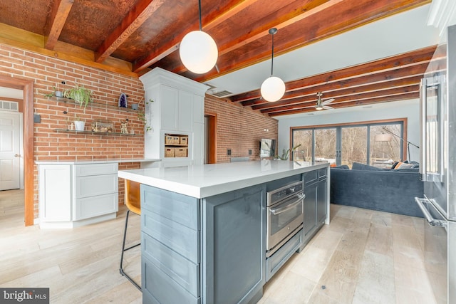 kitchen featuring pendant lighting, appliances with stainless steel finishes, white cabinetry, brick wall, and beamed ceiling