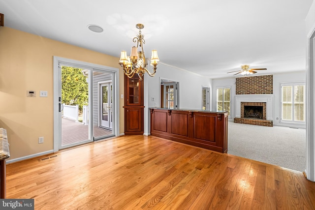 interior space featuring a brick fireplace, ceiling fan with notable chandelier, and light hardwood / wood-style flooring