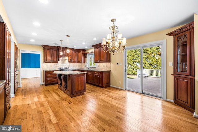 kitchen featuring tasteful backsplash, a notable chandelier, light hardwood / wood-style floors, a kitchen island, and decorative light fixtures