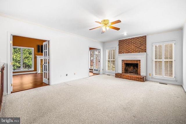 unfurnished living room featuring ceiling fan, ornamental molding, carpet flooring, and a brick fireplace