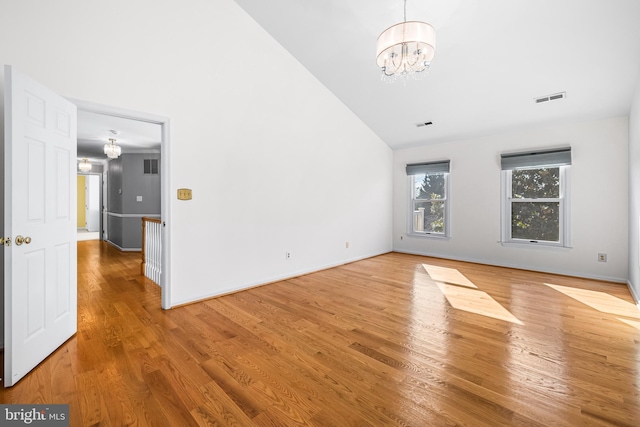 unfurnished living room featuring wood-type flooring, high vaulted ceiling, and an inviting chandelier