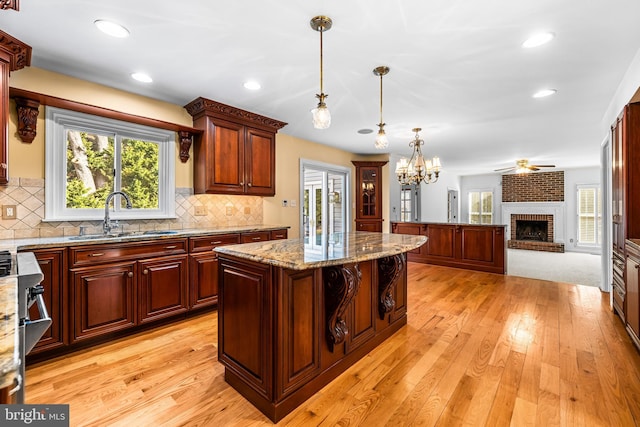 kitchen featuring sink, light stone counters, a kitchen island, pendant lighting, and a fireplace