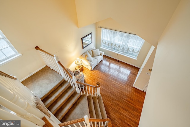 stairway featuring hardwood / wood-style flooring, a healthy amount of sunlight, and a towering ceiling