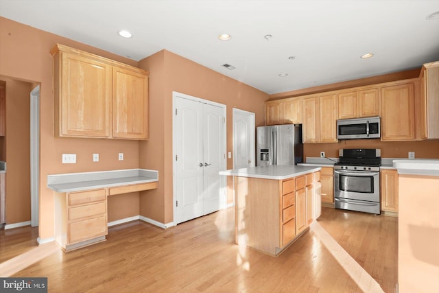 kitchen featuring light brown cabinetry, built in desk, a center island, and appliances with stainless steel finishes