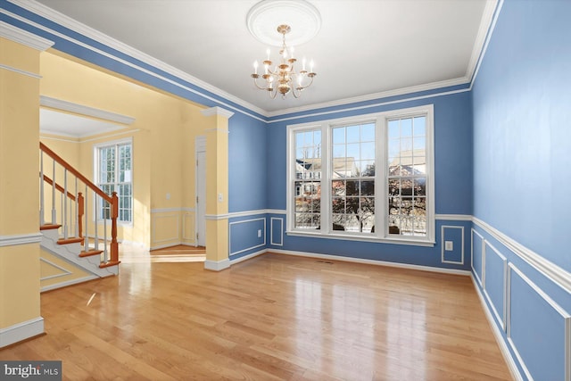 unfurnished dining area featuring an inviting chandelier, ornamental molding, hardwood / wood-style floors, and ornate columns