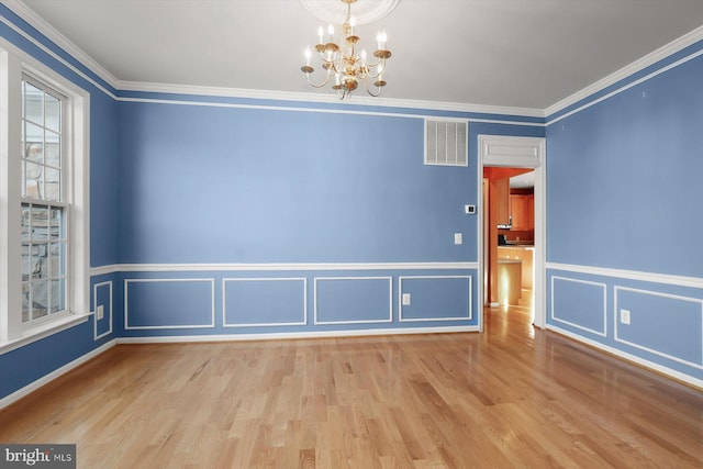 empty room with crown molding, a chandelier, and light wood-type flooring