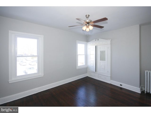 unfurnished room with dark wood-type flooring, ceiling fan, radiator, and a wealth of natural light