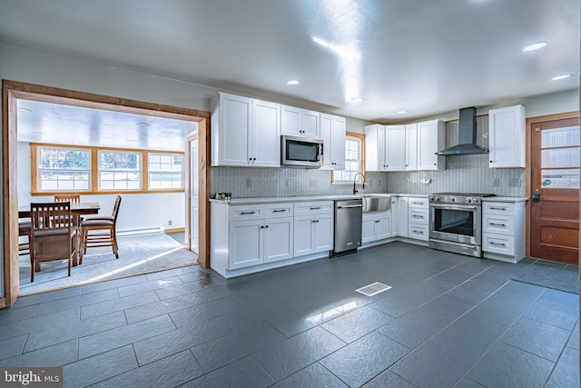 kitchen with wall chimney exhaust hood, sink, tasteful backsplash, appliances with stainless steel finishes, and white cabinets