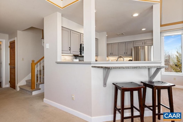 kitchen featuring gray cabinets, a breakfast bar area, stainless steel fridge, light colored carpet, and kitchen peninsula