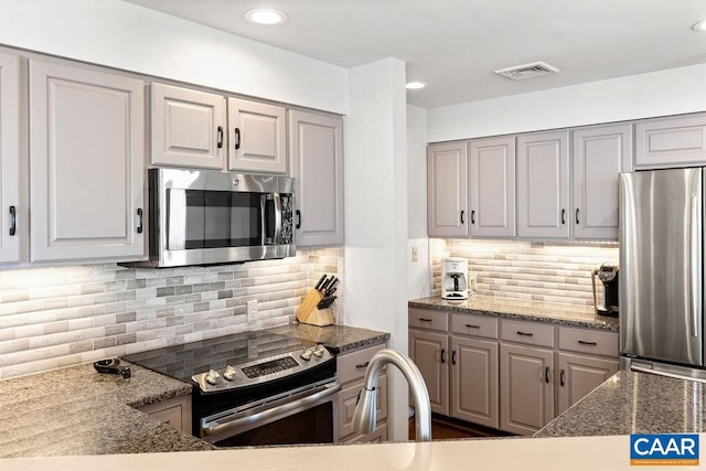 kitchen with tasteful backsplash, appliances with stainless steel finishes, dark stone countertops, and gray cabinetry