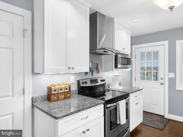 kitchen with white cabinetry, stainless steel appliances, dark stone counters, and wall chimney range hood