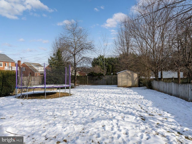 snowy yard featuring a trampoline and a storage shed