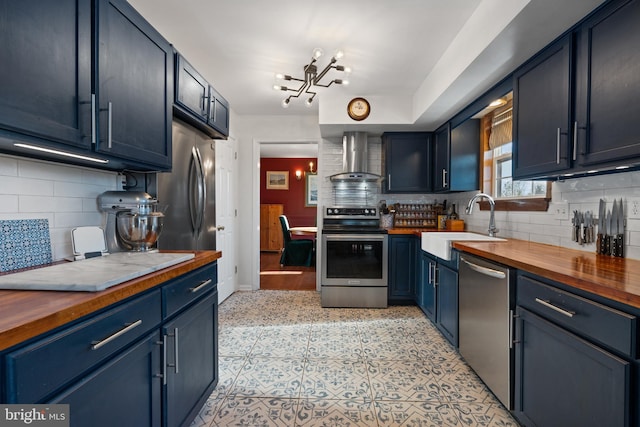 kitchen with stainless steel appliances, wooden counters, wall chimney exhaust hood, and blue cabinets