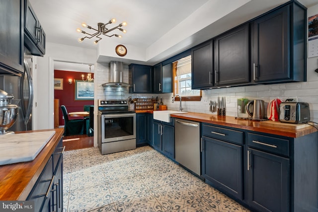 kitchen featuring wood counters, sink, a chandelier, stainless steel appliances, and wall chimney range hood