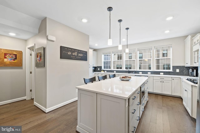 kitchen featuring dark wood-type flooring, white cabinetry, a center island, hanging light fixtures, and decorative backsplash