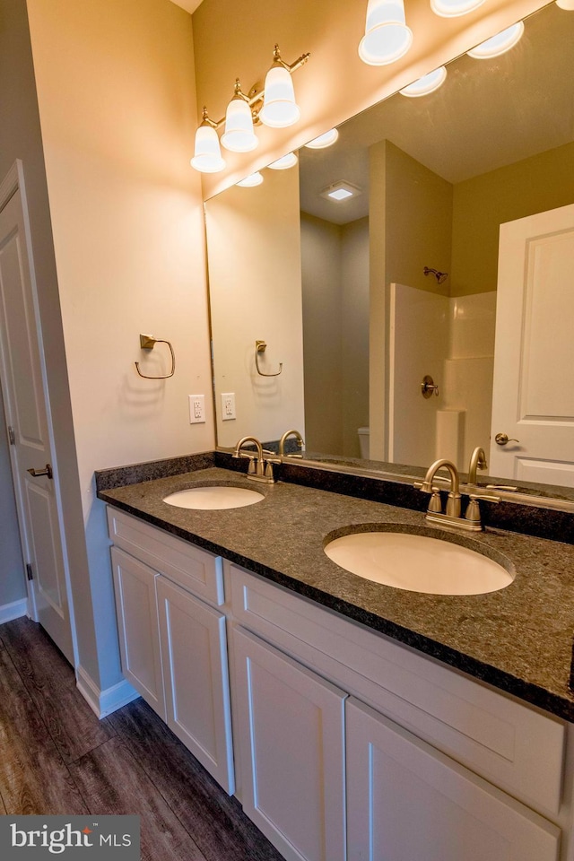 bathroom with double vanity, walk in shower, a sink, and wood finished floors