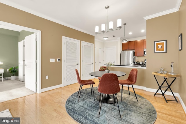 dining space featuring ornamental molding, sink, light hardwood / wood-style flooring, and a notable chandelier