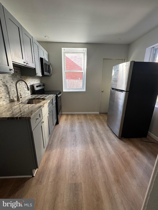 kitchen featuring stainless steel appliances, gray cabinets, sink, and dark stone countertops