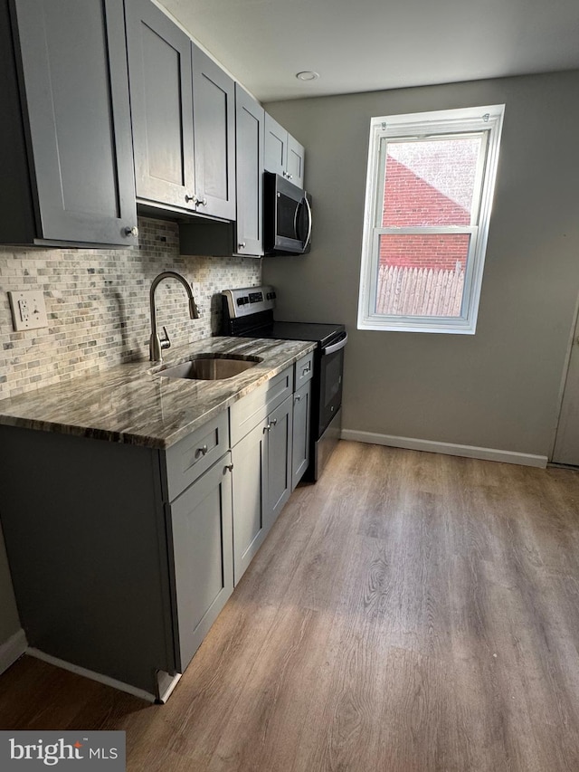 kitchen with sink, dark stone counters, gray cabinets, stainless steel appliances, and backsplash