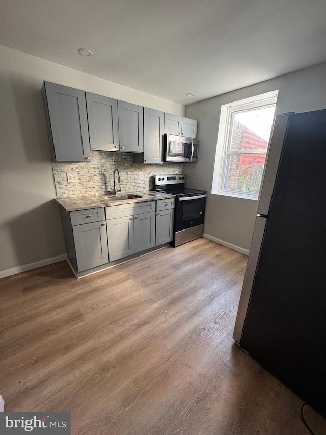 kitchen featuring sink, gray cabinetry, backsplash, light hardwood / wood-style floors, and stainless steel appliances