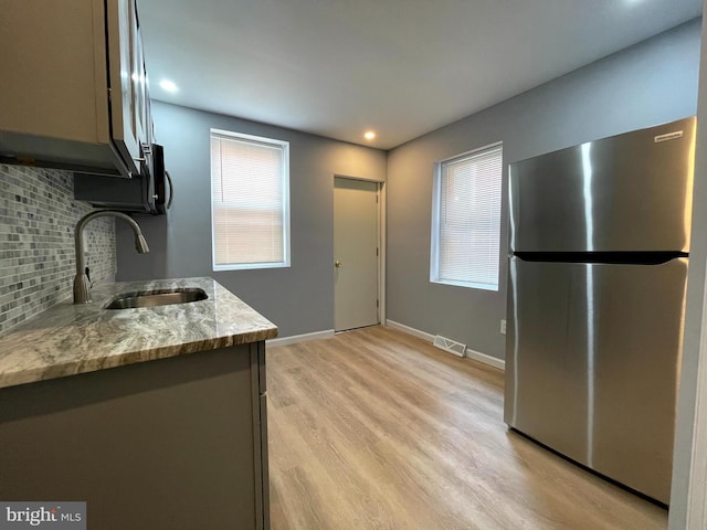 kitchen featuring sink, light stone counters, tasteful backsplash, stainless steel fridge, and light hardwood / wood-style floors