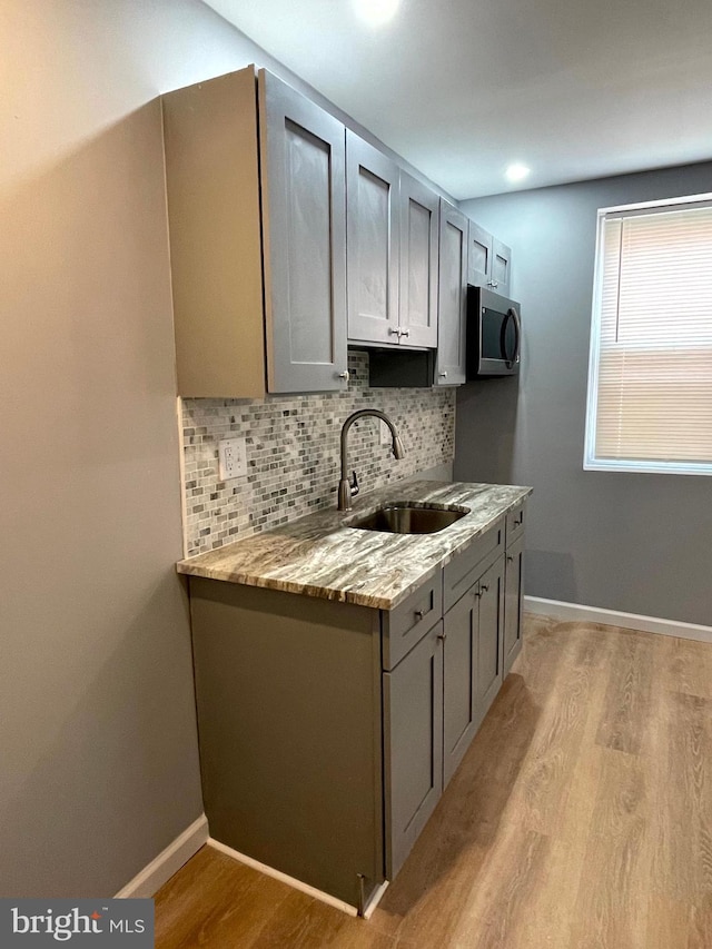 kitchen featuring sink, gray cabinetry, light stone counters, and light hardwood / wood-style flooring