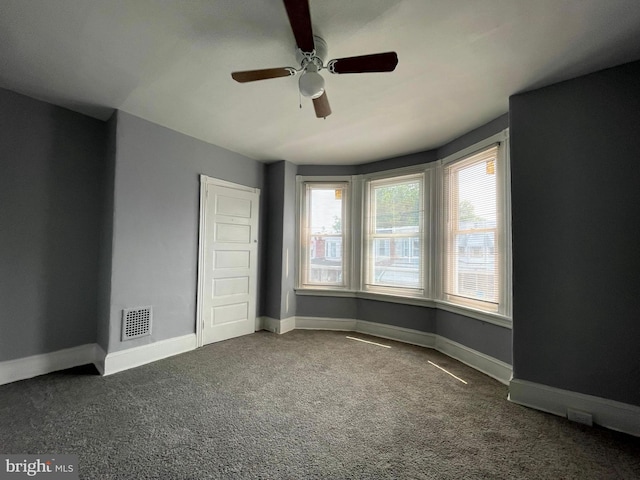 empty room featuring ceiling fan and dark colored carpet