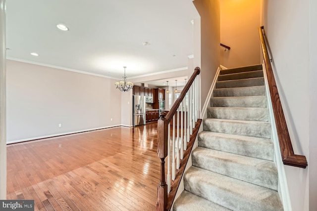 staircase with ornamental molding, hardwood / wood-style floors, and an inviting chandelier