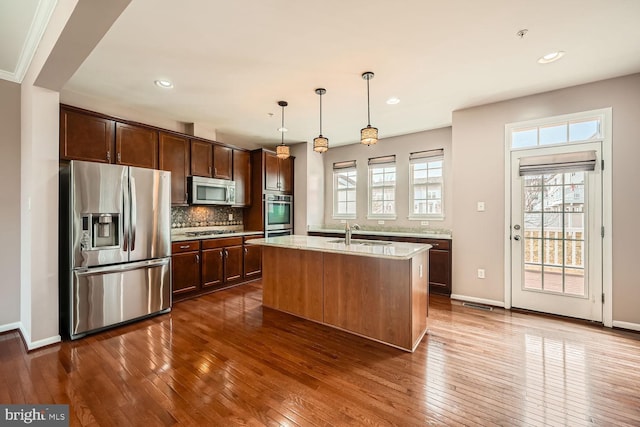 kitchen featuring sink, decorative light fixtures, an island with sink, stainless steel appliances, and light stone countertops