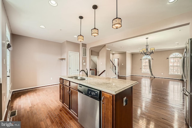 kitchen with dark wood-type flooring, sink, appliances with stainless steel finishes, an island with sink, and pendant lighting