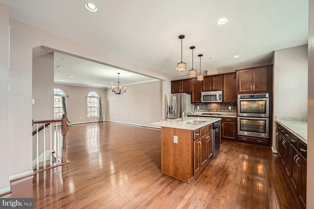 kitchen featuring decorative light fixtures, sink, stainless steel appliances, light stone countertops, and a center island with sink