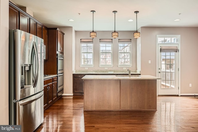 kitchen featuring an island with sink, appliances with stainless steel finishes, sink, and decorative light fixtures