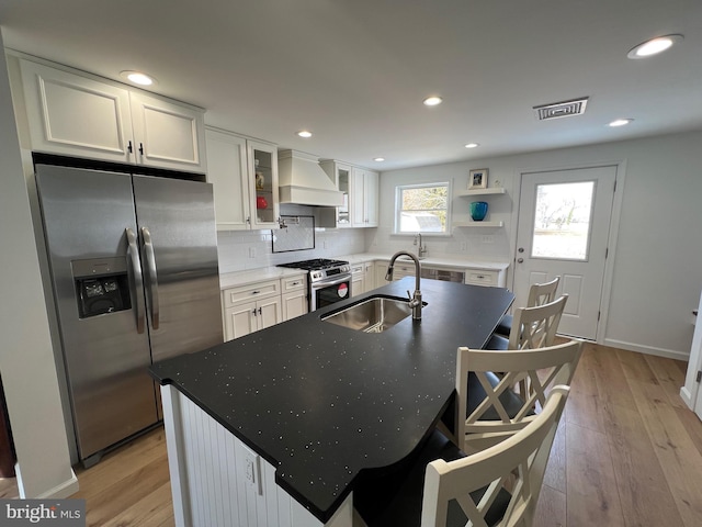 kitchen with white cabinetry, sink, custom exhaust hood, stainless steel appliances, and a center island with sink