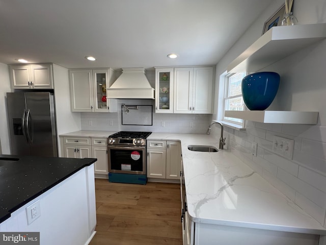 kitchen with sink, premium range hood, stainless steel appliances, light stone counters, and white cabinets