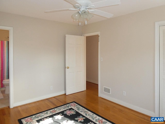 unfurnished bedroom with ceiling fan, ensuite bathroom, and wood-type flooring