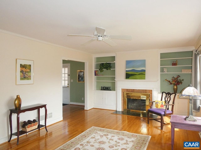 living room featuring hardwood / wood-style flooring, ornamental molding, built in features, and a fireplace